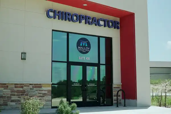 Exterior entrance of a chiropractic clinic in Fort Worth, TX, with prominent chiropractor signage, glass doors, and modern building facade.